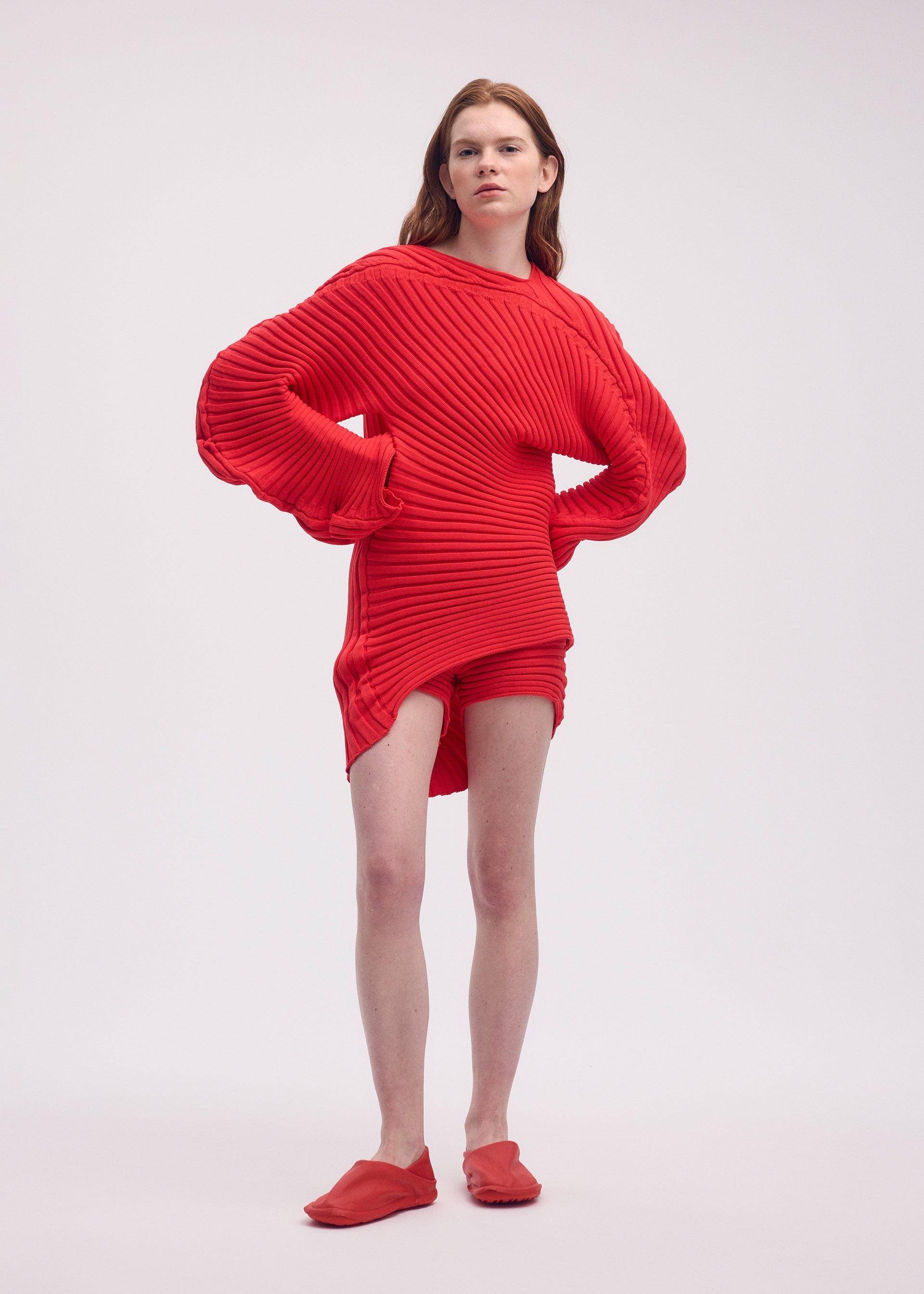Person wearing a red ribbed sweater and matching slippers on a white background