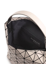 A close-up of the VALLEY handbag by BAO BAO ISSEY MIYAKE shows its geometric-patterned gusset, wide handle, black interior lining, and inner pocket with a branded label. The bag stands upright for easy access.