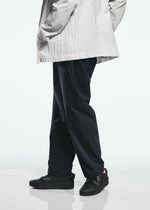 Wearing the TYPE-S BASICS black sneakers from A-POC ABLE ISSEY MIYAKE, the person is dressed in cropped pants and a light-colored, pleated-detail jacket, photographed from the shoulders down against a plain background.