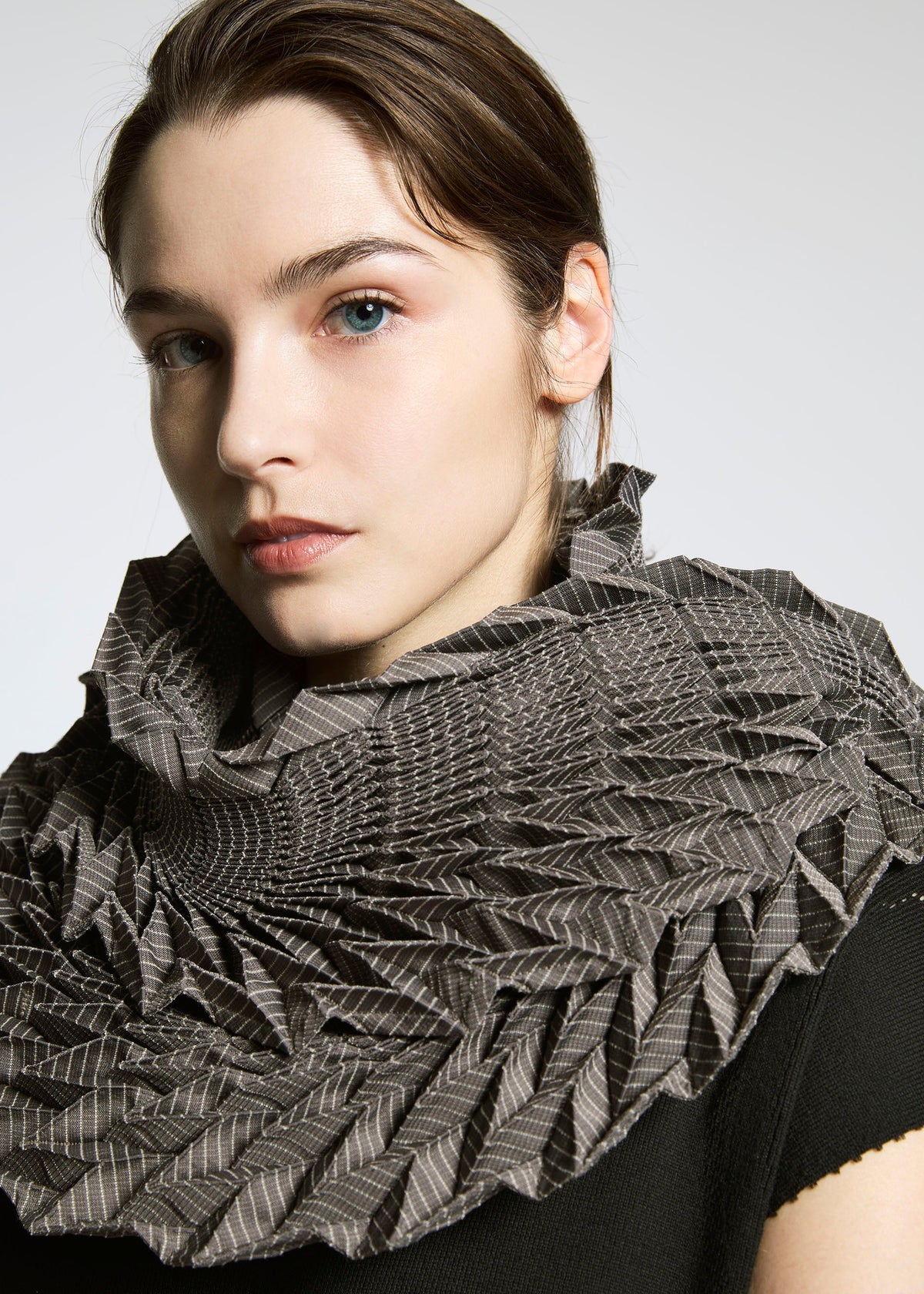 A woman with light skin and brown hair wears the TYPE-O STOLE by A-POC ABLE ISSEY MIYAKE over a black top. The stole features a three-dimensional geometric pattern. She gazes to the side against a plain light background. view 10 of 17