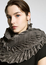 A woman with light skin and brown hair wears the TYPE-O STOLE by A-POC ABLE ISSEY MIYAKE over a black top. The stole features a three-dimensional geometric pattern. She gazes to the side against a plain light background.
