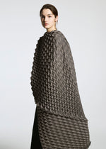 A woman models the TYPE-O STOLE by A-POC ABLE ISSEY MIYAKE—a textured, geometric-patterned gray and black cape with a voluminous scarf—looking at the camera against a plain light gray background.