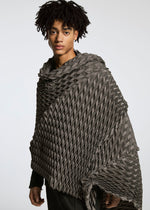 A person with short, curly hair wears the gray TYPE-O STOLE by A-POC ABLE ISSEY MIYAKE, featuring a three-dimensional pattern, standing before a plain light background and looking calmly at the camera.