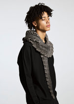 A person with short curly hair models the TYPE-O STOLE by A-POC ABLE ISSEY MIYAKE, featuring a voluminous 3D-patterned scarf and a black sweater, standing against a plain light background with a neutral expression.