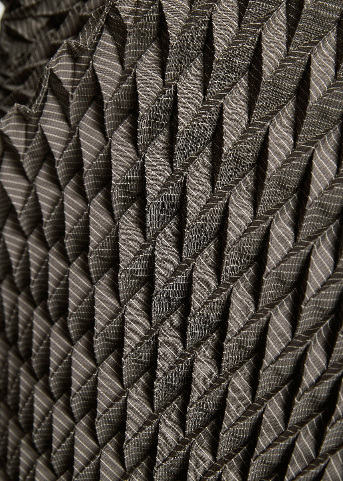 Close-up of the TYPE-O STOLE by A-POC ABLE ISSEY MIYAKE, showcasing its geometric 3D pleated pattern in grey tones with textured folds and bold diagonal lines. view 15 of 17