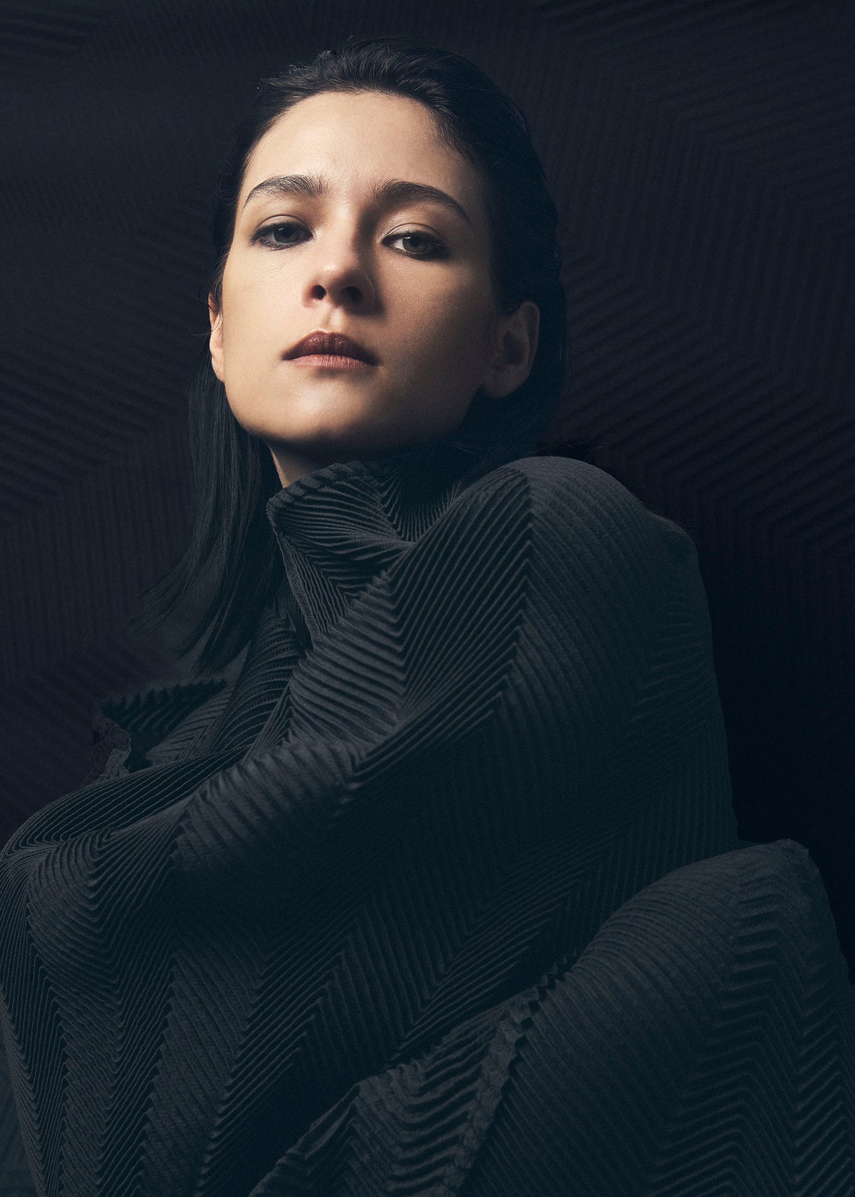 A woman with dark hair and bold makeup gazes confidently at the camera, wrapped in TYPE-XIV Eugene Studio project 002 by A-POC ABLE ISSEY MIYAKE, as dramatic “Light and Shadow Inside Me” lighting casts bold shadows on her face and clothing. view 5 of 11