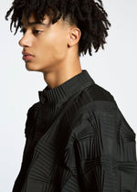 A person with short, curly hair wears the TYPE-O 018 pleated black jacket by A-POC ABLE ISSEY MIYAKE, featuring a high collar and large buttons, looking left against a plain white background.