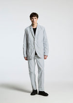 A person with short, dark hair and a neutral expression stands facing forward against a plain white background, wearing the TYPE-U 001 jacket by A-POC ABLE ISSEY MIYAKE, styled with a black shirt and black shoes.