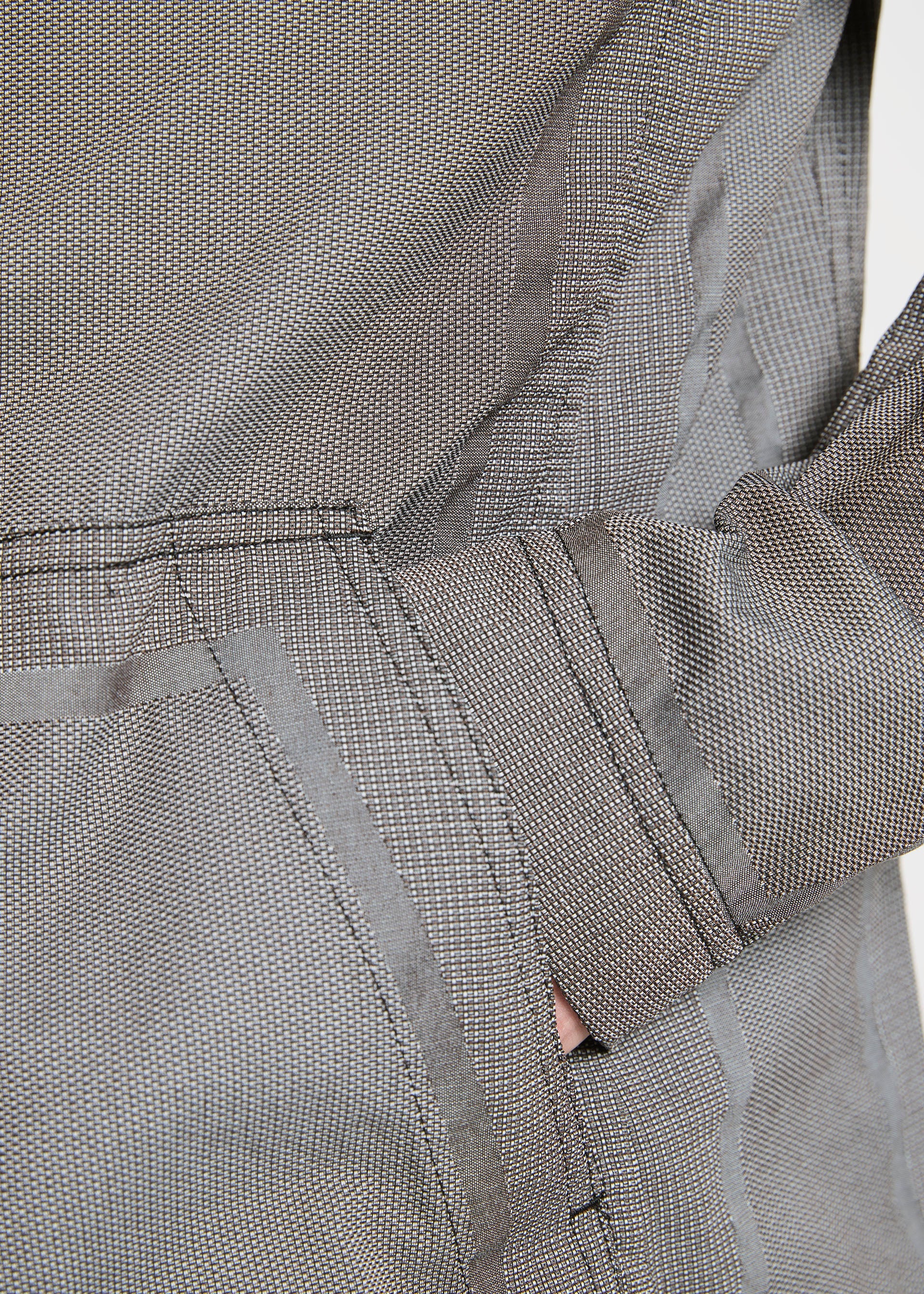 Zoomed view Close-up of a person wearing the TYPE-U 001 relaxed fit jacket by A-POC ABLE ISSEY MIYAKE in textured gray. One hand is partly tucked into a side pocket. The fabric has a fine checkered pattern and visible stitching for detail.