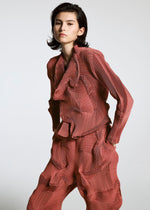 A person with short dark hair wears the TYPE-O 003 BK by A-POC ABLE ISSEY MIYAKE, a matching red textured set with a long-sleeve top and loose pants featuring wavy, sculpted details, standing against a plain light background.