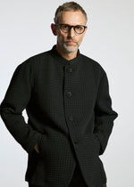 A man with short gray hair, a beard, and black-rimmed glasses wears the TYPE-O 014 standing collar jacket by A-POC ABLE ISSEY MIYAKE, posing with hands in pockets against a light gray background.