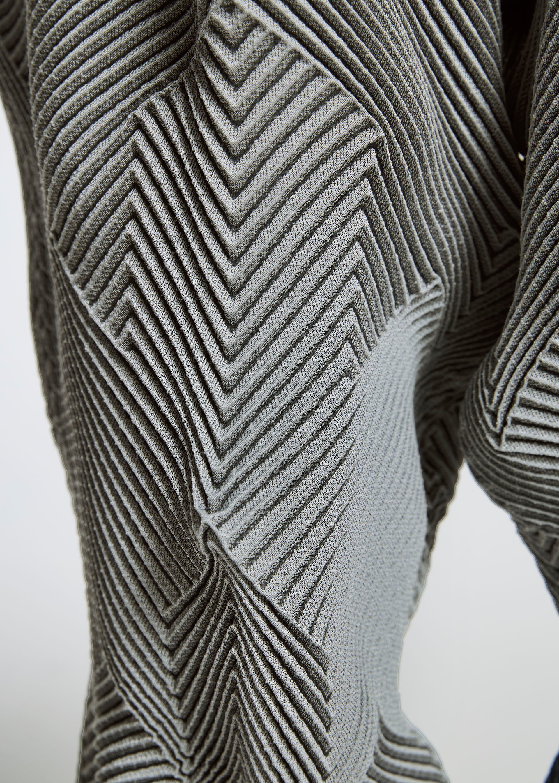 Zoomed view Close-up of TYPE-O 010 by A-POC ABLE ISSEY MIYAKE: gray recycled polyester fabric featuring a raised, geometric zigzag and chevron pattern for a textured, three-dimensional surface.