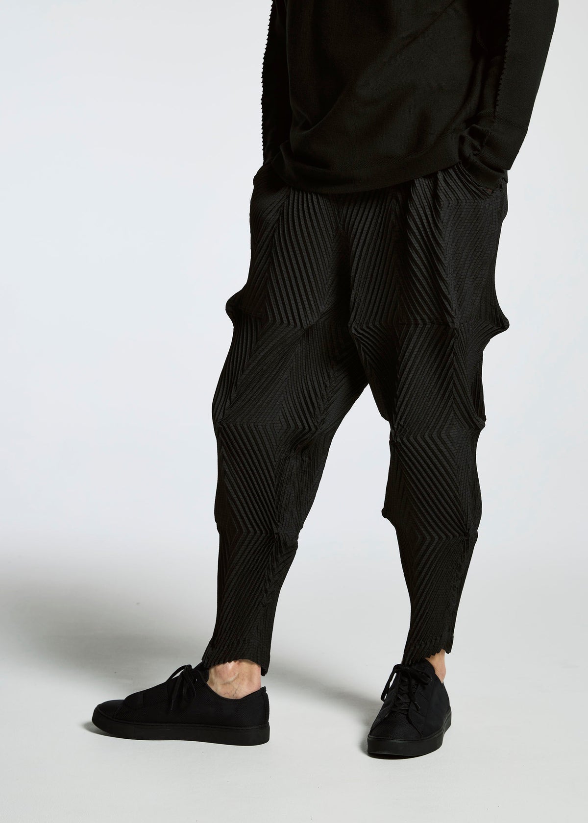 A person wears TYPE-O 007 textured black pants by A-POC ABLE ISSEY MIYAKE, featuring a geometric pattern, paired with black sneakers and a long-sleeve black top, standing against a plain white background. view 6 of 10