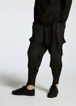 A person wears TYPE-O 007 textured black pants by A-POC ABLE ISSEY MIYAKE, featuring a geometric pattern, paired with black sneakers and a long-sleeve black top, standing against a plain white background.