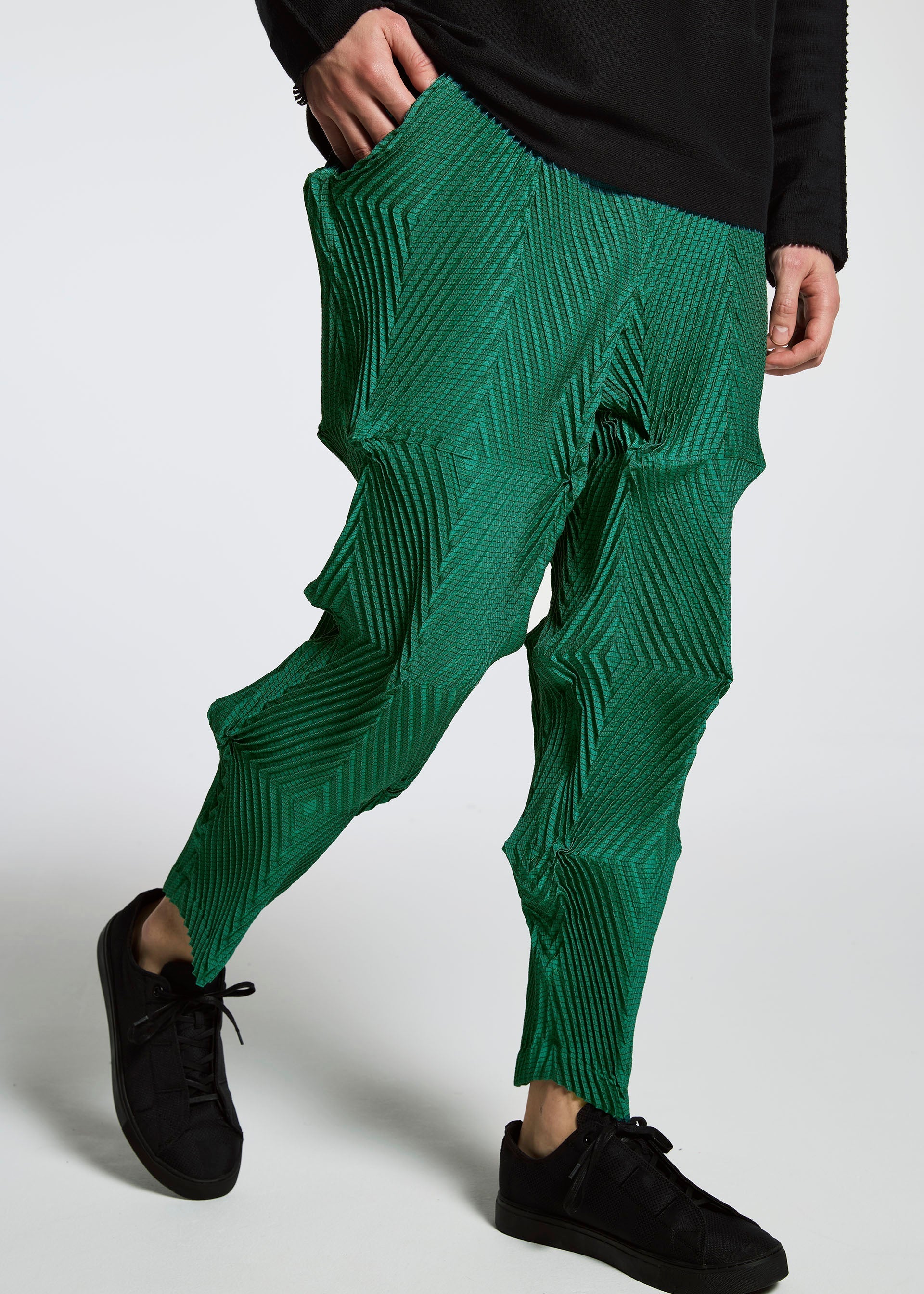 Zoomed view A person wears TYPE-O 007 bright green pleated pants with geometric patterns by A-POC ABLE ISSEY MIYAKE, paired with a black top and sneakers. The photo is cropped from shoulders down against a plain white background.
