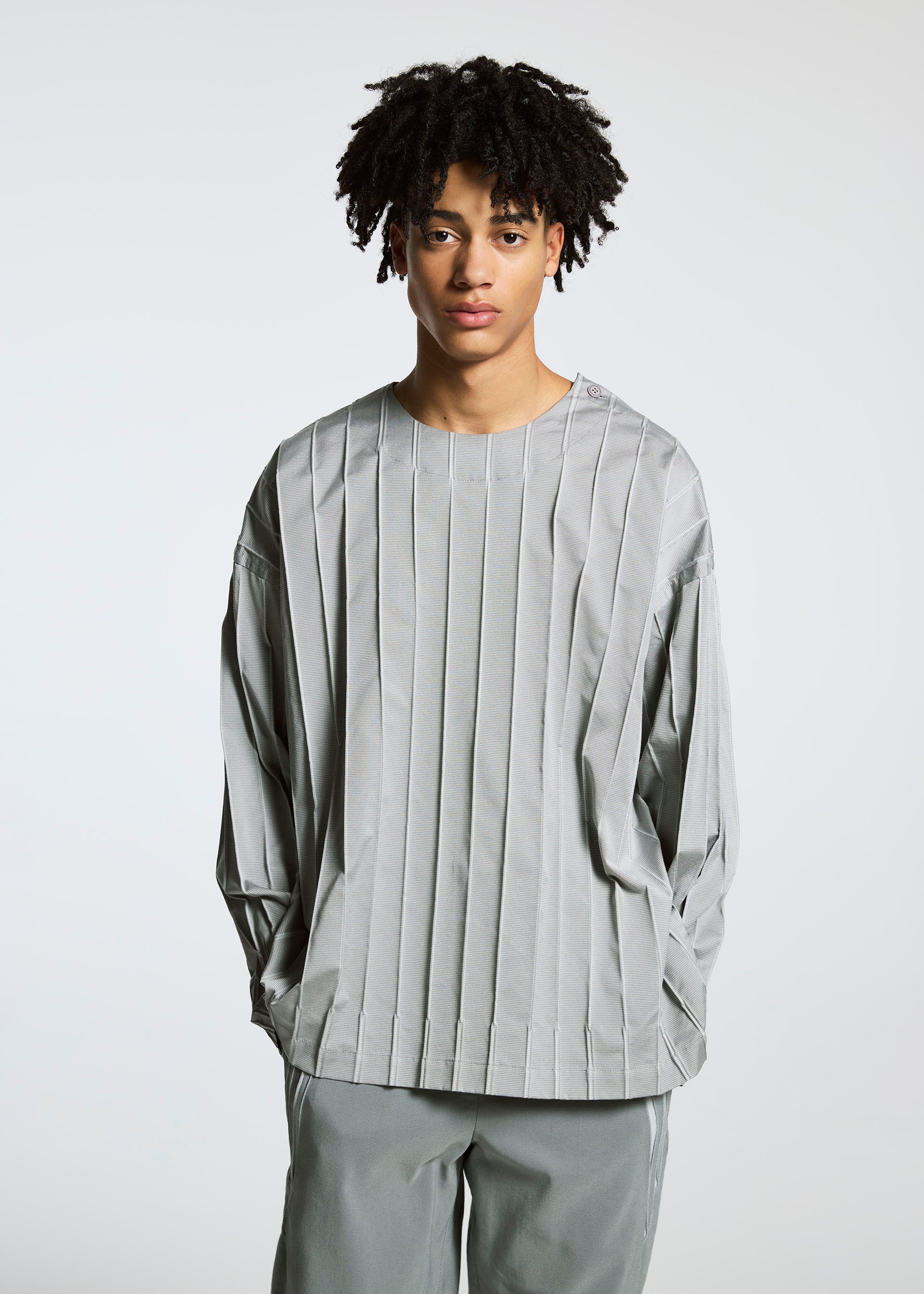 Zoomed view A youth with short curly hair wears TYPE-C 003 by A-POC ABLE ISSEY MIYAKE: a loose, light gray striped long-sleeve top and matching pants, standing against a plain white background.