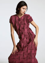 Someone poses against a plain background wearing the TYPE-O 018 short-sleeved, textured maroon dress with geometric raised square patterns and steam stretch detailing by A-POC ABLE ISSEY MIYAKE.