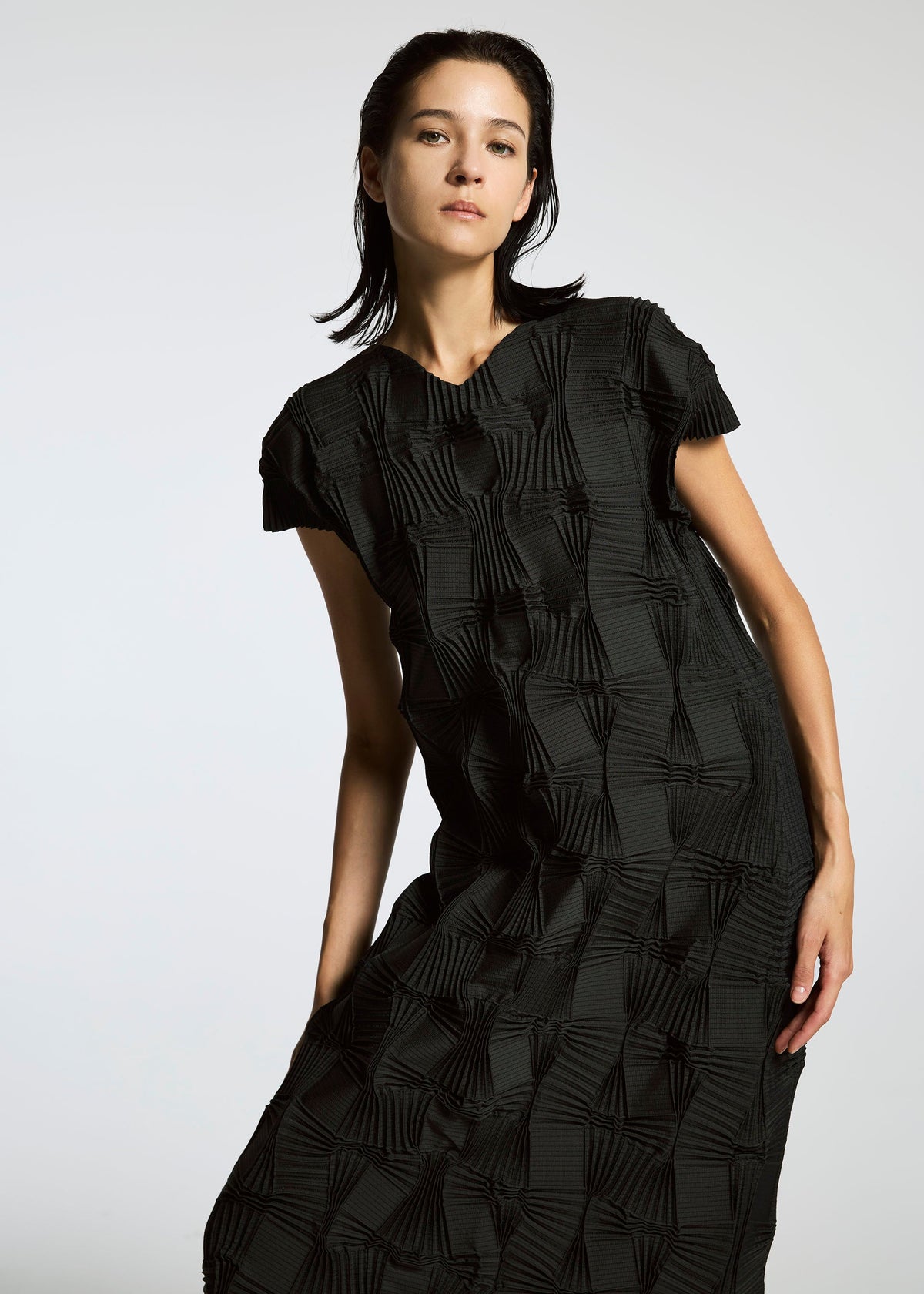 A person with dark, slicked-back hair models the TYPE-O 018 pleated black dress by A-POC ABLE ISSEY MIYAKE against a plain light background, highlighting its textured fabric and subtle Steam Stretch detailing. view 6 of 6