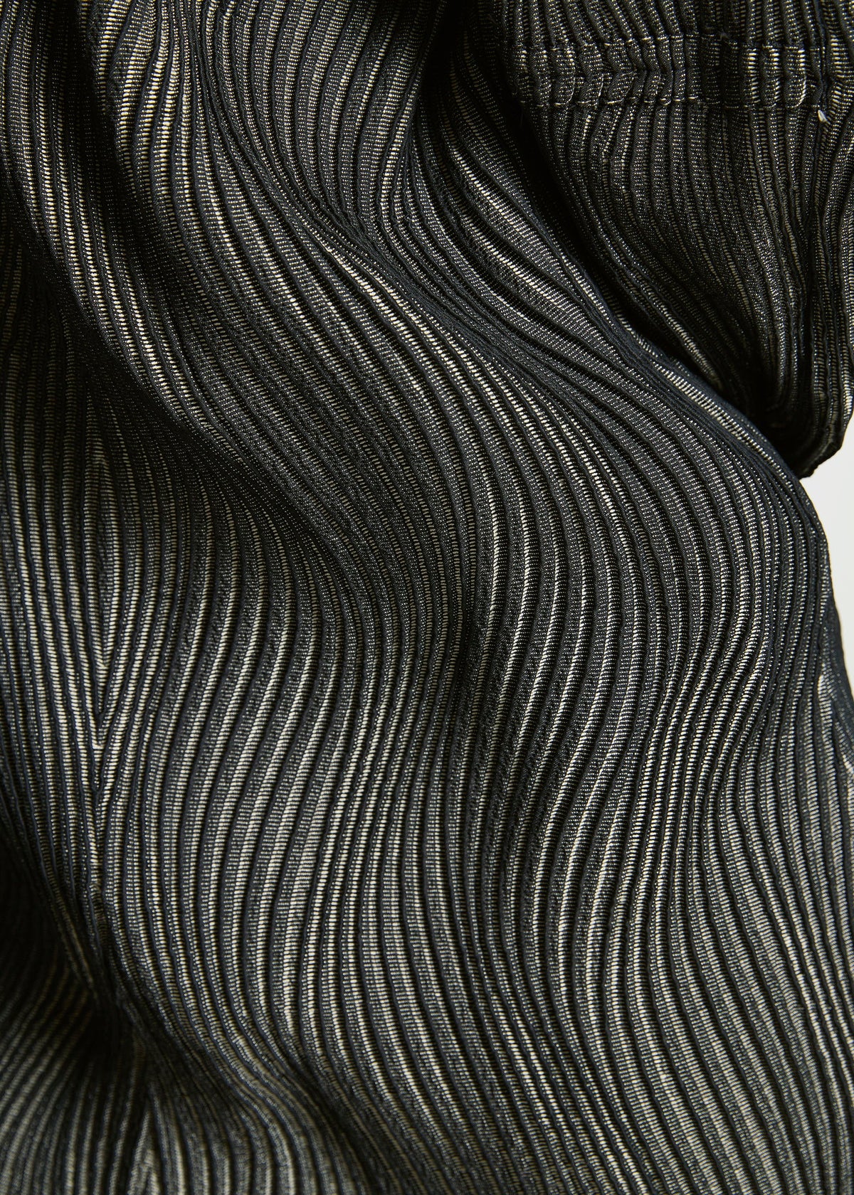 Close-up of black, pleated fabric from TYPE-XI Spiber project by A-POC ABLE ISSEY MIYAKE, showing intricate wavy texture and fine lines. Lighting highlights the contours and sheen of this innovative biodegradable material. view 7 of 7