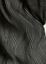 Close-up of black TYPE-XI Spiber project Brewed Protein™ fiber fabric by A-POC ABLE ISSEY MIYAKE, featuring a wavy, pleated texture with fine light lines creating a rippling pattern across the surface.