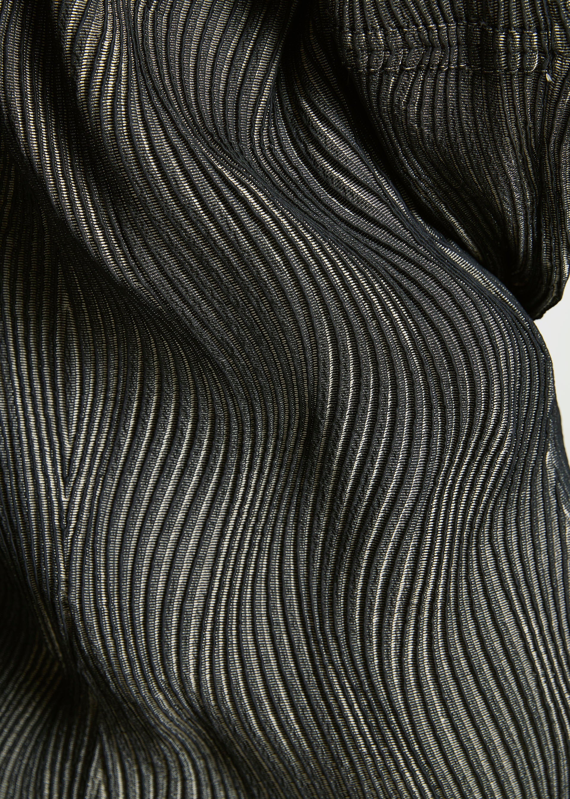 Zoomed view Close-up of black TYPE-XI Spiber project Brewed Protein™ fiber fabric by A-POC ABLE ISSEY MIYAKE, featuring a wavy, pleated texture with fine light lines creating a rippling pattern across the surface.