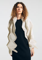 A person with curly hair wears a black dress and the TYPE-O STOLE 002 by A-POC ABLE ISSEY MIYAKE, a white geometric jacket with origami zigzag folds, standing against a plain light background.