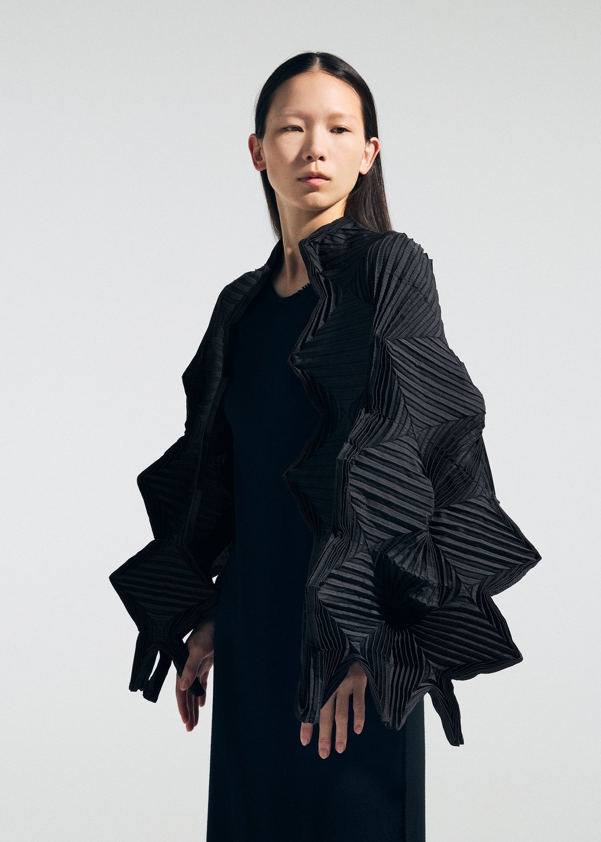A person with straight dark hair wears a black dress and the TYPE-O STOLE 002 by A-POC ABLE ISSEY MIYAKE, featuring large geometric ruffles reminiscent of origami folds, against a plain light background. view 14 of 15