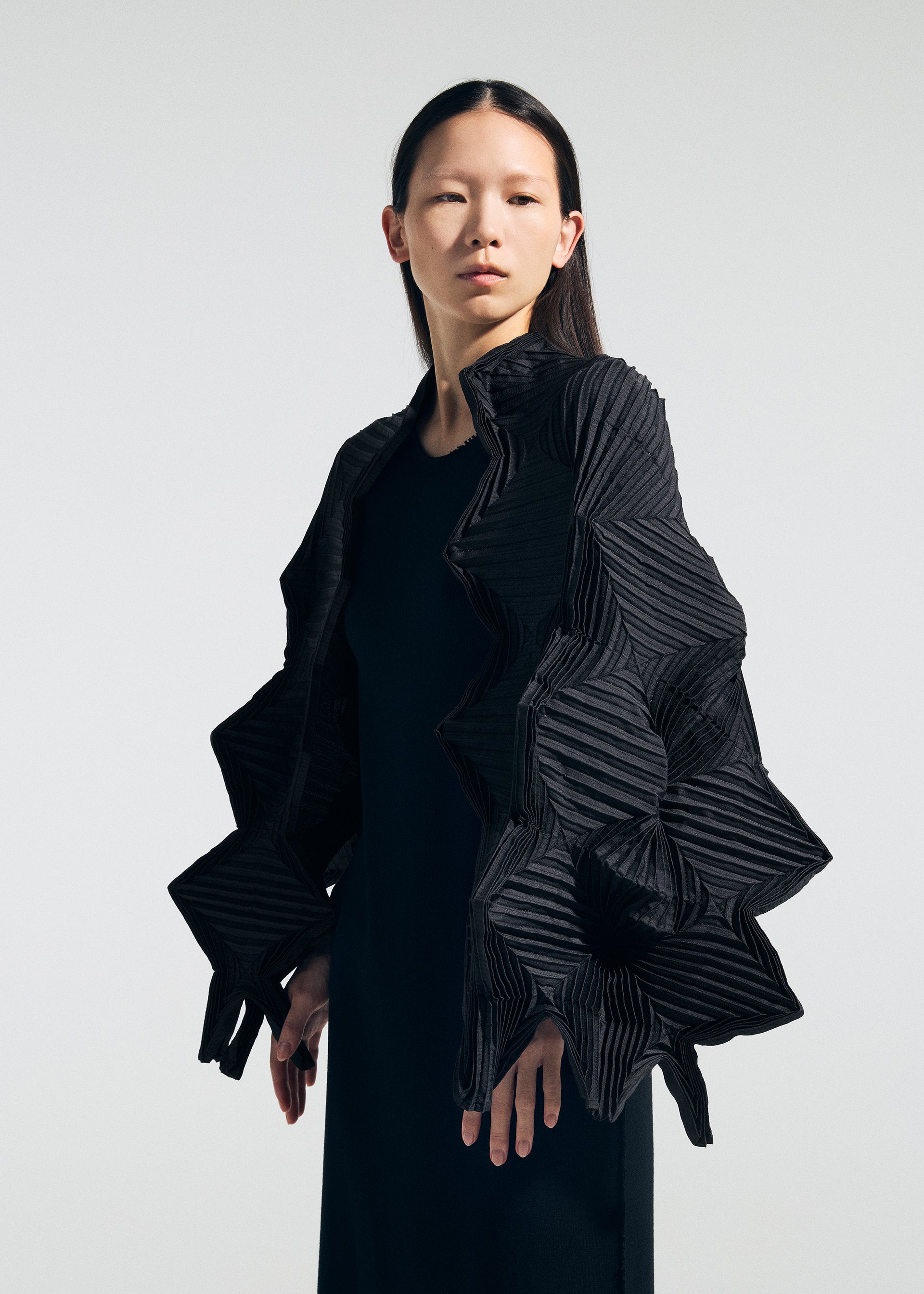 Zoomed view A person with straight dark hair wears a black dress and the TYPE-O STOLE 002 by A-POC ABLE ISSEY MIYAKE, featuring large geometric ruffles reminiscent of origami folds, against a plain light background.