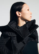 A woman with straight dark hair, shown in profile against a plain light background, wears a black outfit featuring the TYPE-O STOLE 002 by A-POC ABLE ISSEY MIYAKE, styled with dramatic pleated origami folds around her shoulders and neck.