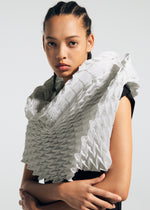 A person with braided hair wears a black top and TYPE-Ⅶ Kouzoshi project 002—a sculptural, geometric white collar crafted from folded material inspired by Tosa Washi paper by A-POC ABLE ISSEY MIYAKE—while standing against a plain background with a serious expression.