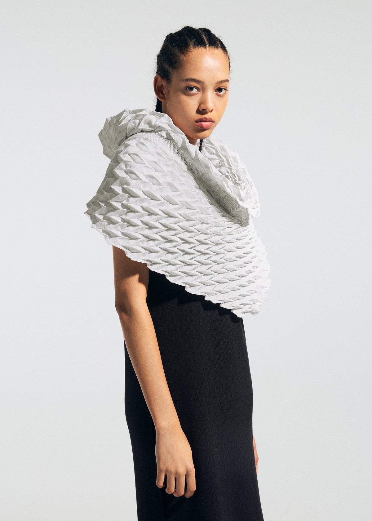 A person in a black sleeveless dress drapes the sculptural, geometric white TYPE-Ⅶ Kouzoshi project 002 stole by A-POC ABLE ISSEY MIYAKE—crafted from Tosa Washi paper—around their shoulders, gazing neutrally at the camera against a plain background. view 13 of 15