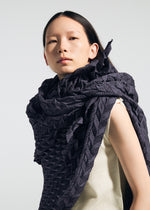 A person with long dark hair wears a textured, sculptural TYPE-Ⅶ Kouzoshi project 002 stole from A-POC ABLE ISSEY MIYAKE, draped over a sleeveless cream top, looking confidently at the camera against a plain light background.