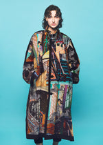 A person wearing a long, colorful coat inspired by contemporary art fashion, featuring an intricate cityscape pattern with figures, buildings, stairs, and zebras—a striking TYPE-XII Tomokazu Matsuyama project 003 coat from A-POC ABLE ISSEY MIYAKE—posing against a plain turquoise background.