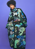 A person wearing a long, colorful TYPE-XII Tomokazu Matsuyama project 003 coat by A-POC ABLE ISSEY MIYAKE, featuring bold abstract patterns in green, blue, and black, stands against a purple background with hands in pockets, gazing at the camera—a striking statement of contemporary art fashion.