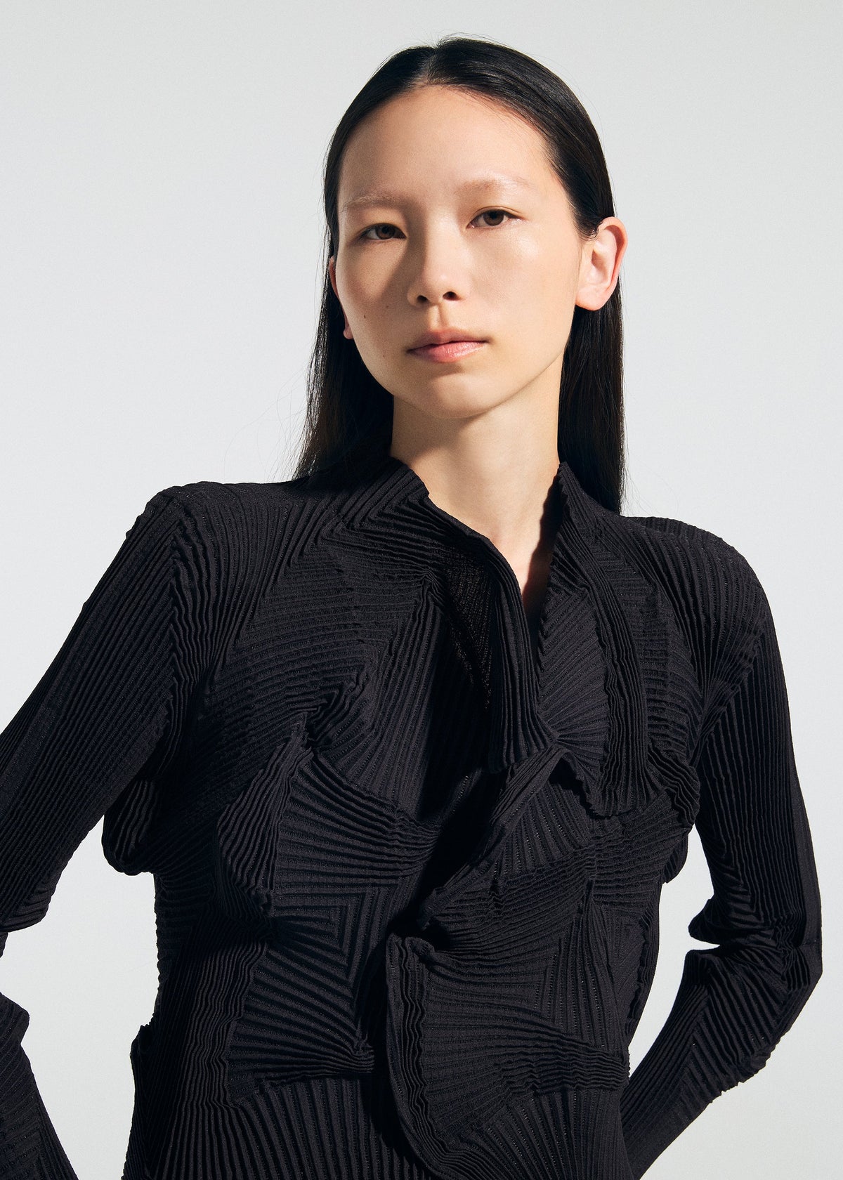 A person with long, straight dark hair models the TYPE-O 022 jacket by A-POC ABLE ISSEY MIYAKE—featuring a high collar and geometric patterns—standing against a plain light background and looking confidently at the camera. view 8 of 8