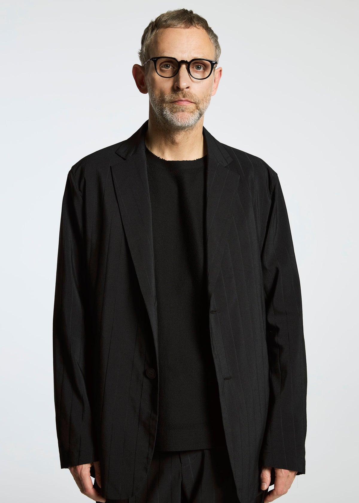 A man with short gray hair, glasses, and a beard wears the TYPE-Ⅰ 007 jacket by A-POC ABLE ISSEY MIYAKE over a black shirt, standing against a plain white background. view 5 of 5