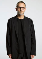 A man with short gray hair, glasses, and a beard wears the TYPE-Ⅰ 007 jacket by A-POC ABLE ISSEY MIYAKE over a black shirt, standing against a plain white background.