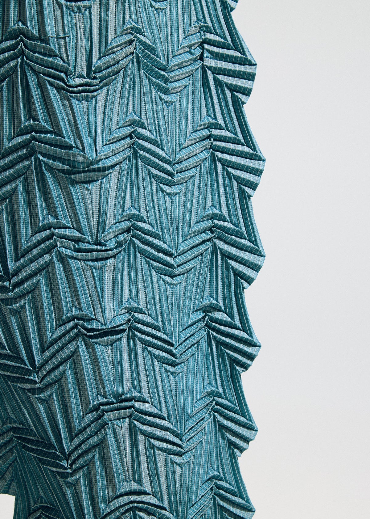 Close-up of TYPE-O 019 by A-POC ABLE ISSEY MIYAKE: blue fabric with geometric, zigzag, and layered patterns. The structured, three-dimensional effect resembles zigzag pleat pants crafted with the Steam Stretch technique. view 11 of 11
