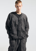 A person with short, light hair stands against a plain background, hands in pockets, wearing the TYPE-O 010 jacket and pleated houndstooth pants by A-POC ABLE ISSEY MIYAKE.