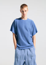 A person with short blond hair stands against a plain light background, wearing the TYPE-W 009-1 by A-POC ABLE ISSEY MIYAKE, hands in their pockets and looking directly at the camera.