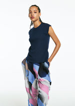 A woman with braided hair stands against a white background wearing the TYPE-XV SOAR NY project 001 pants by A-POC ABLE ISSEY MIYAKE, featuring loose pleats and a wavy pattern, her hands in her pockets.