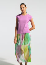 A woman wears the TYPE-P 005 skirt by A-POC ABLE ISSEY MIYAKE, featuring a wavy texture and vivid green, yellow, and pink colors, along with a sleeveless lavender top against a plain light background.