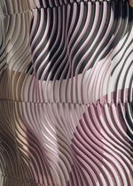 A close-up of TYPE-P 005 fabric by A-POC ABLE ISSEY MIYAKE shows wavy pleats and abstract patterns in pink, black, beige, and white. Dynamic lines create a Baked Stretch effect for striking depth and movement.