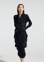 A woman with long dark hair wears the TYPE-O 022 dress by A-POC ABLE ISSEY MIYAKE, featuring black textured fabric, ruffled details, and an antibacterial skirt, standing against a plain light background.