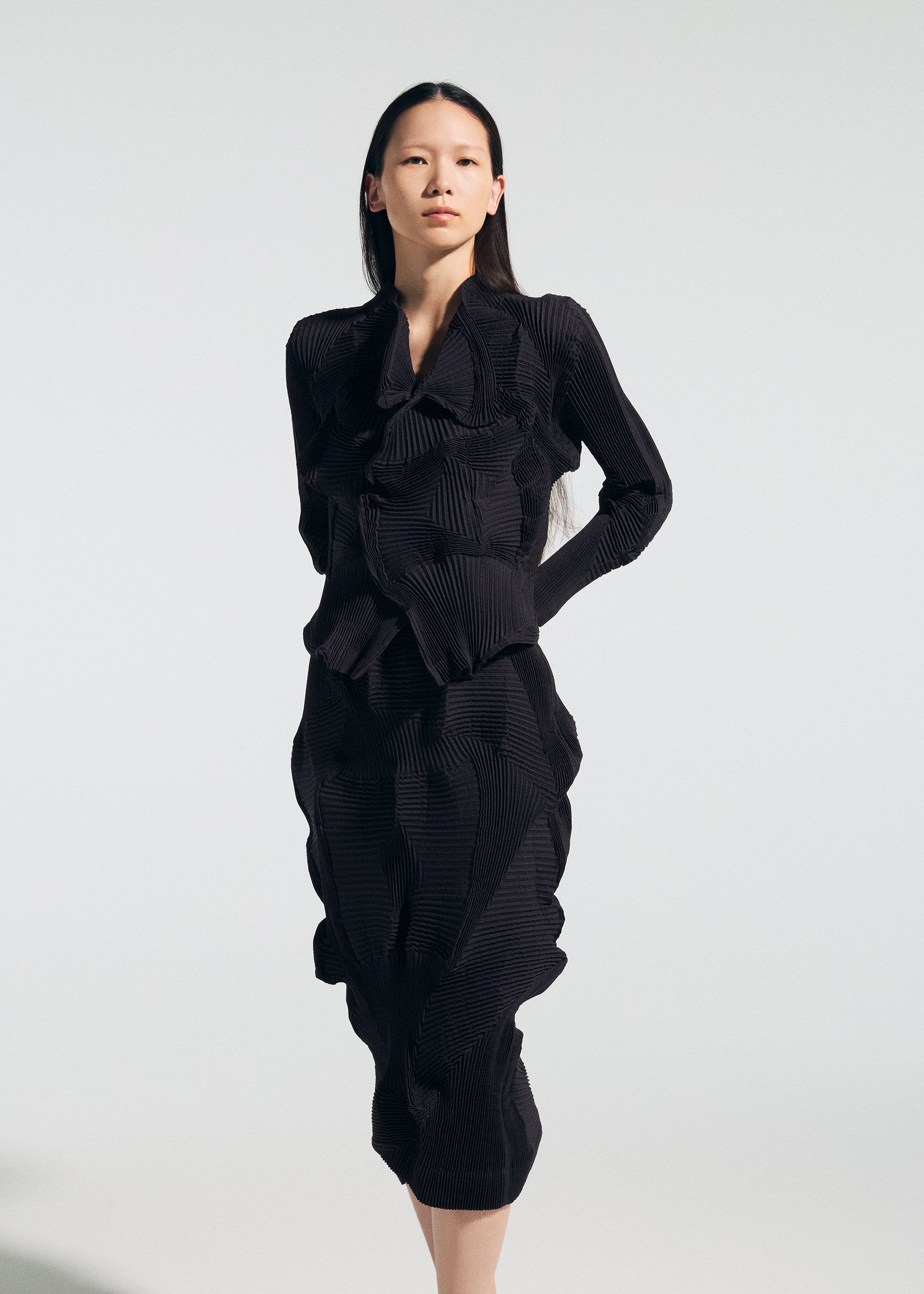 Zoomed view A woman with long dark hair wears the TYPE-O 022 dress by A-POC ABLE ISSEY MIYAKE, featuring black textured fabric, ruffled details, and an antibacterial skirt, standing against a plain light background.