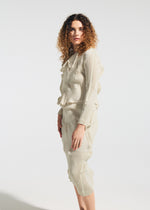 A woman with curly hair models the TYPE-O 022 textured long-sleeve top and pleated skirt by A-POC ABLE ISSEY MIYAKE, standing against a white background and gazing confidently at the camera.