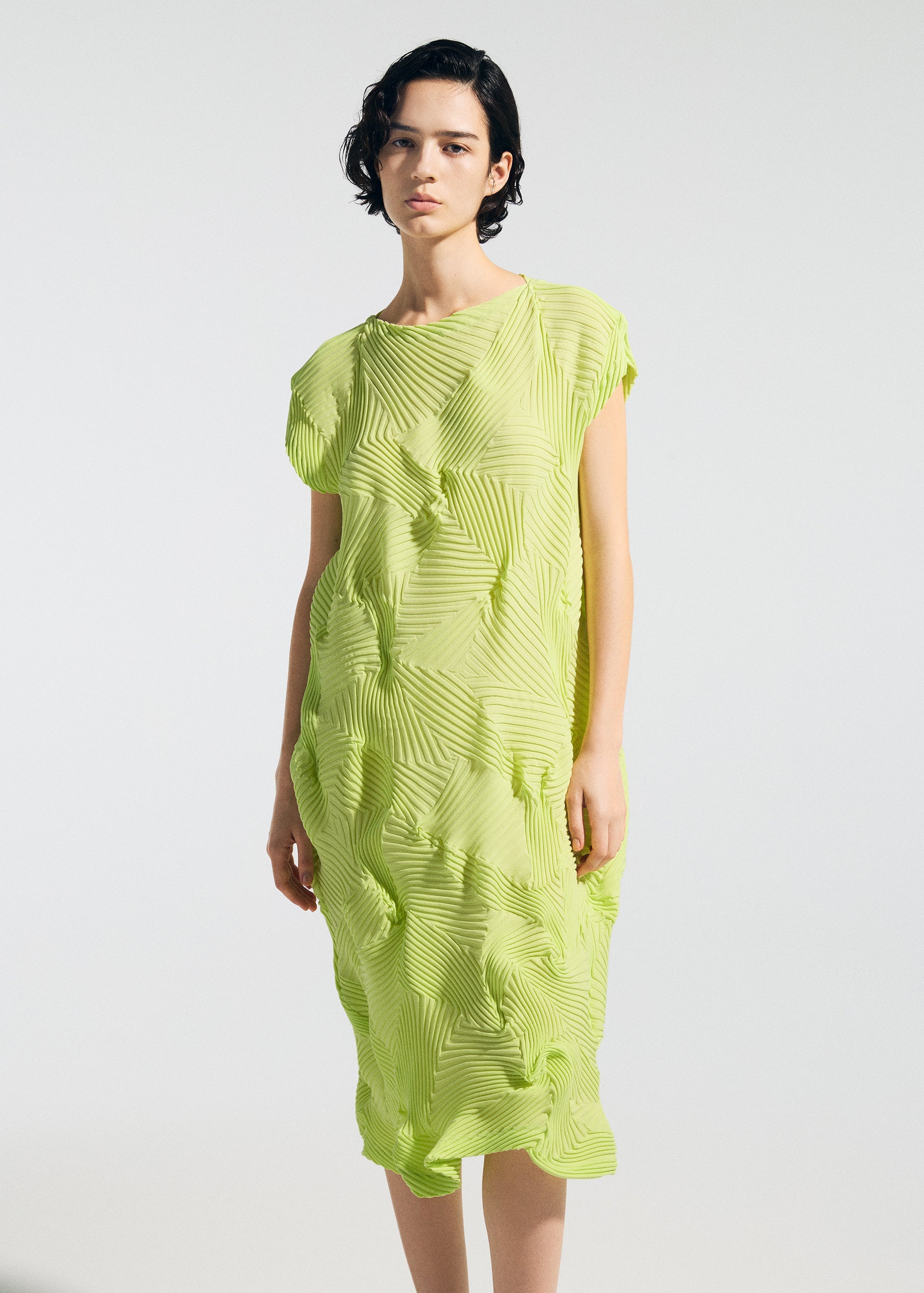 Zoomed view A person with short dark hair wears the TYPE-P 003-2 by A-POC ABLE ISSEY MIYAKE, a loose lime-green pleated dress with a geometric textured pattern, standing against a plain background—perfect for versatile everyday wear.