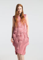 A woman with long, straight, reddish-brown hair stands against a plain light background, wearing the TYPE-O 003 BK dress by A-POC ABLE ISSEY MIYAKE—a sleeveless piece with an intricate geometric texture that's comfortable year-round.