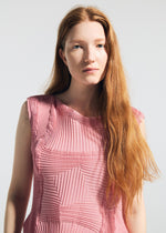 A woman with long red hair models the TYPE-O 003 BK sleeveless textured pink top by A-POC ABLE ISSEY MIYAKE, standing against a plain light background and looking calmly at the camera.