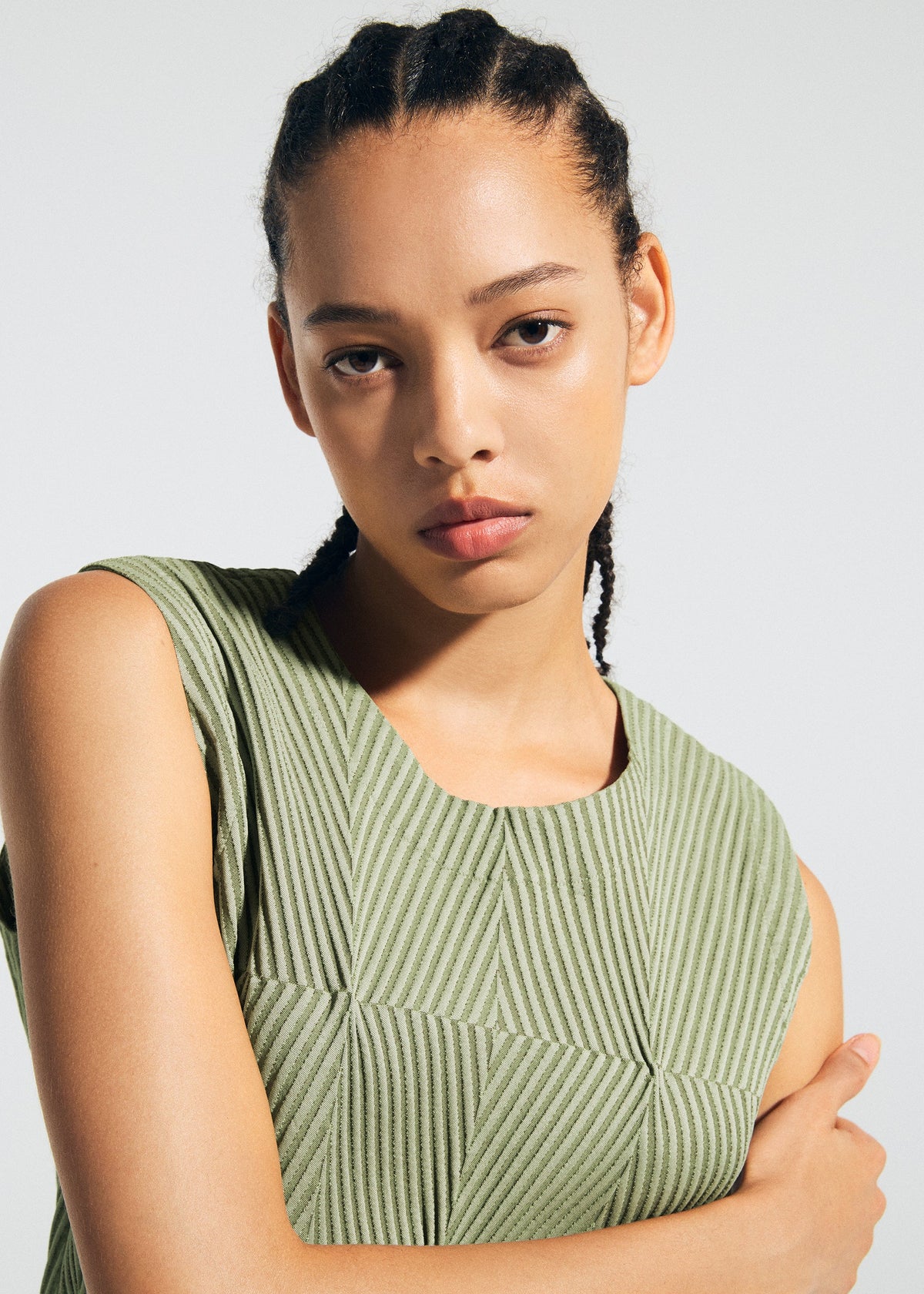 A person with braided hair and a serious expression wears the textured, sleeveless green TYPE-W 009-2 dress by A-POC ABLE ISSEY MIYAKE, standing against a plain light background. view 8 of 10